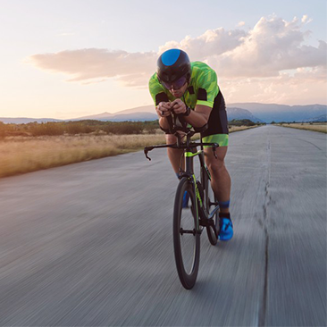 cyclist riding a time trial bike on morning workout sunset or sunrise in background